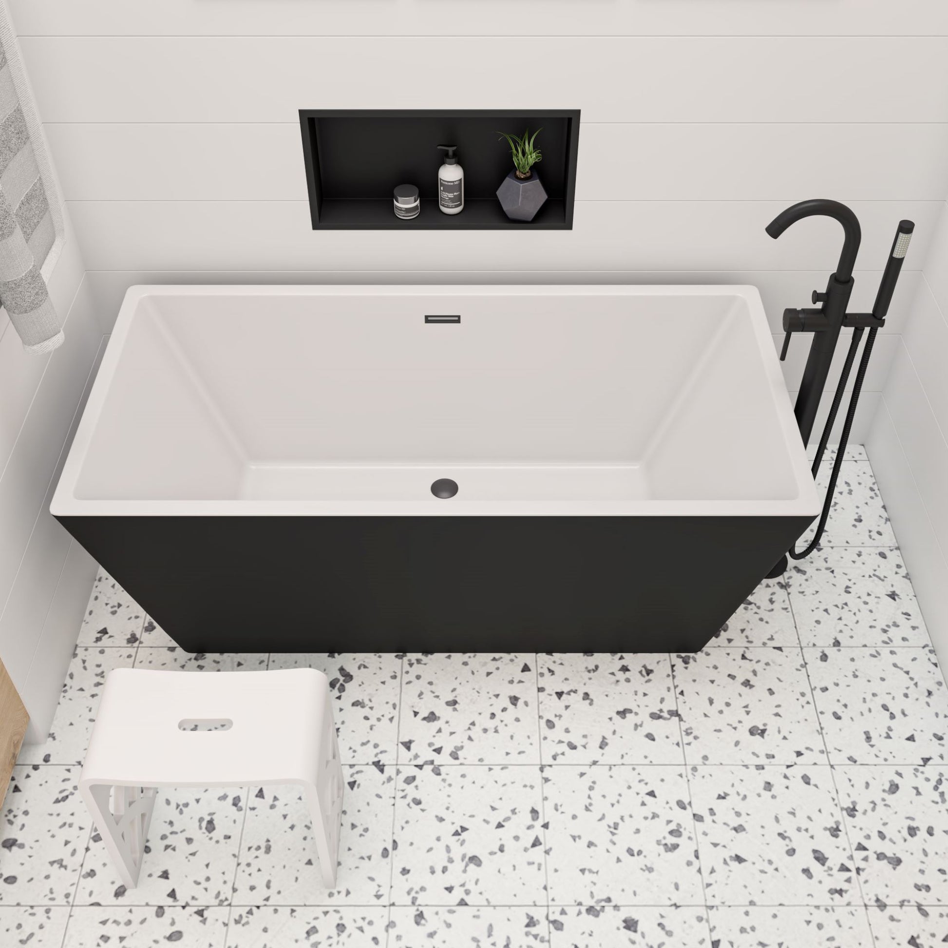 ALFI Brand Modern black freestanding bathtub in a bathroom with white stool and terrazzo flooring. - Luxe Tub Source