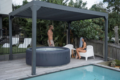 Two people by a hot tub under a pergola next to a pool.
