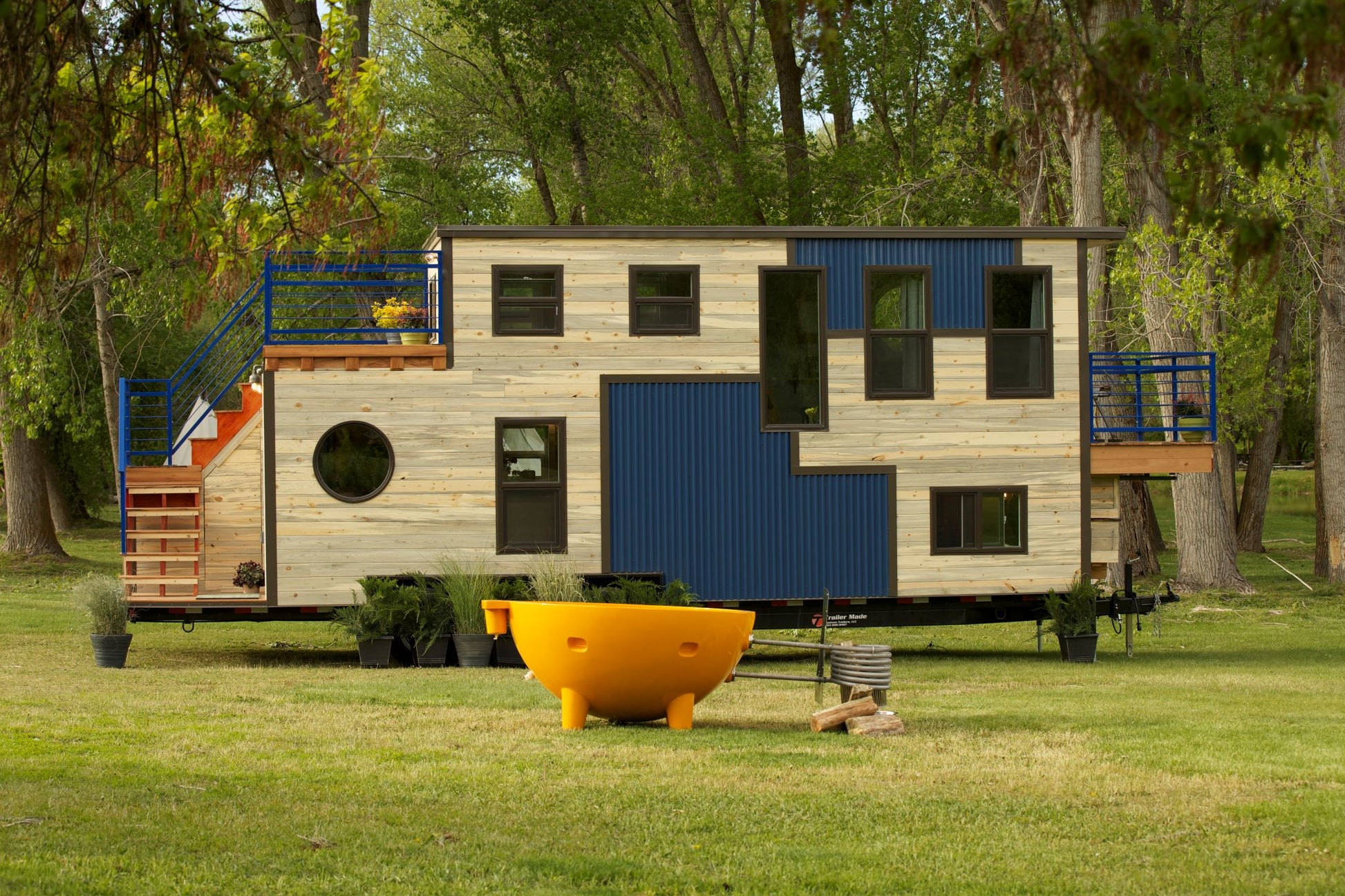 ALFI Brand Yellow Outdoor Wood-Burning Hot Tub in front of a Modular house on wheels with geometric design - Luxe Tub Source