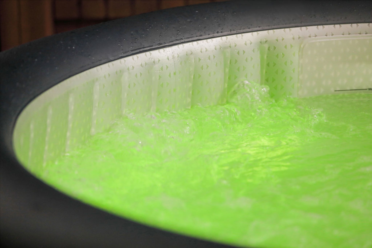 Close-up of an inflatable hot tub filled with water, and green LED lights are shining through the water.