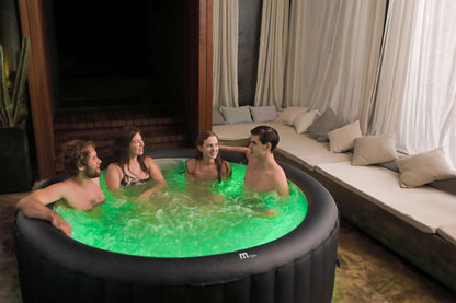 Four people in a hot tub with green lighting in a cozy indoor setting.