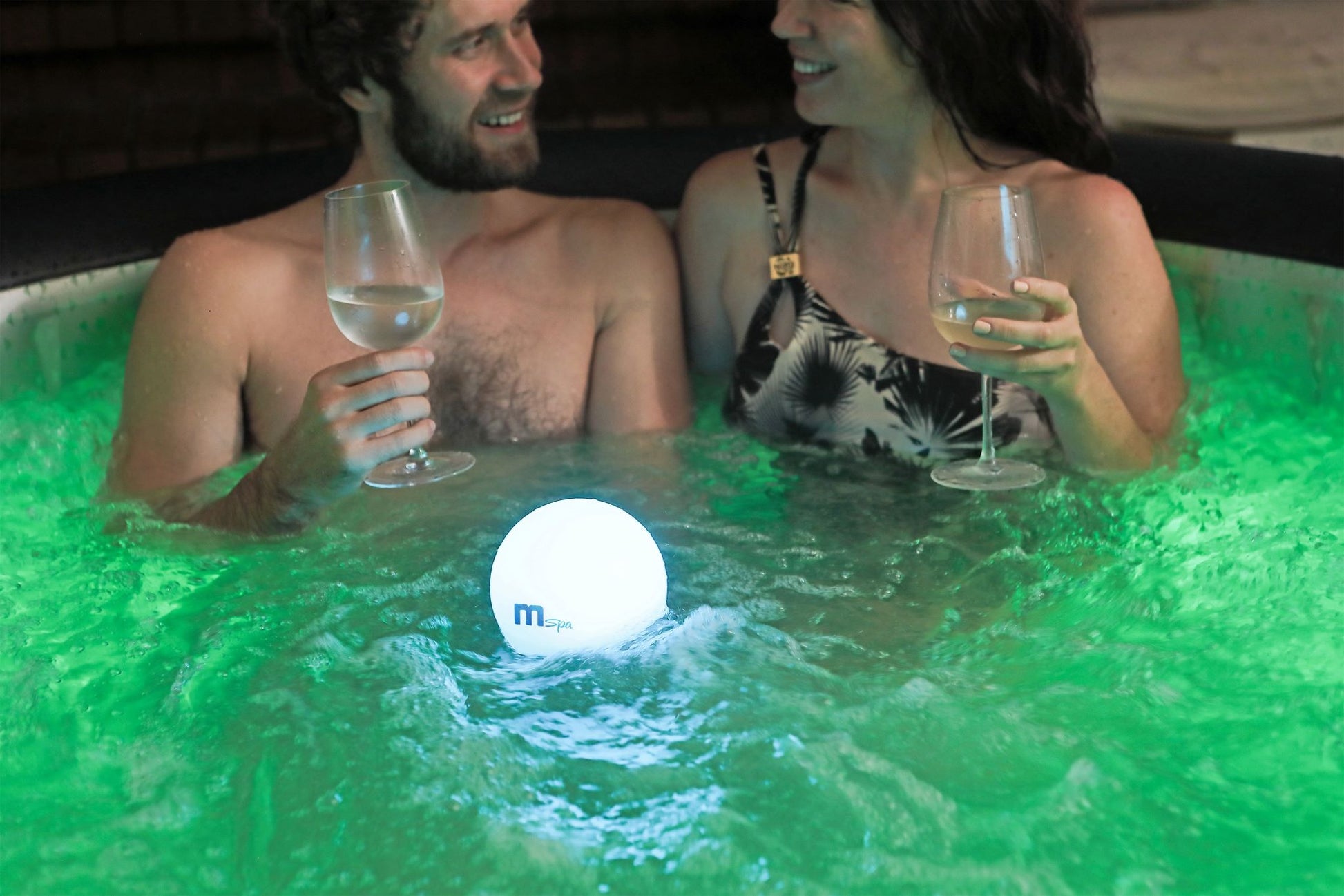Two people in a hot tub with a glowing light bulb floating in the water.