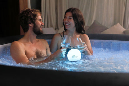 Man and woman in a hot tub with a glowing sphere and drinks.