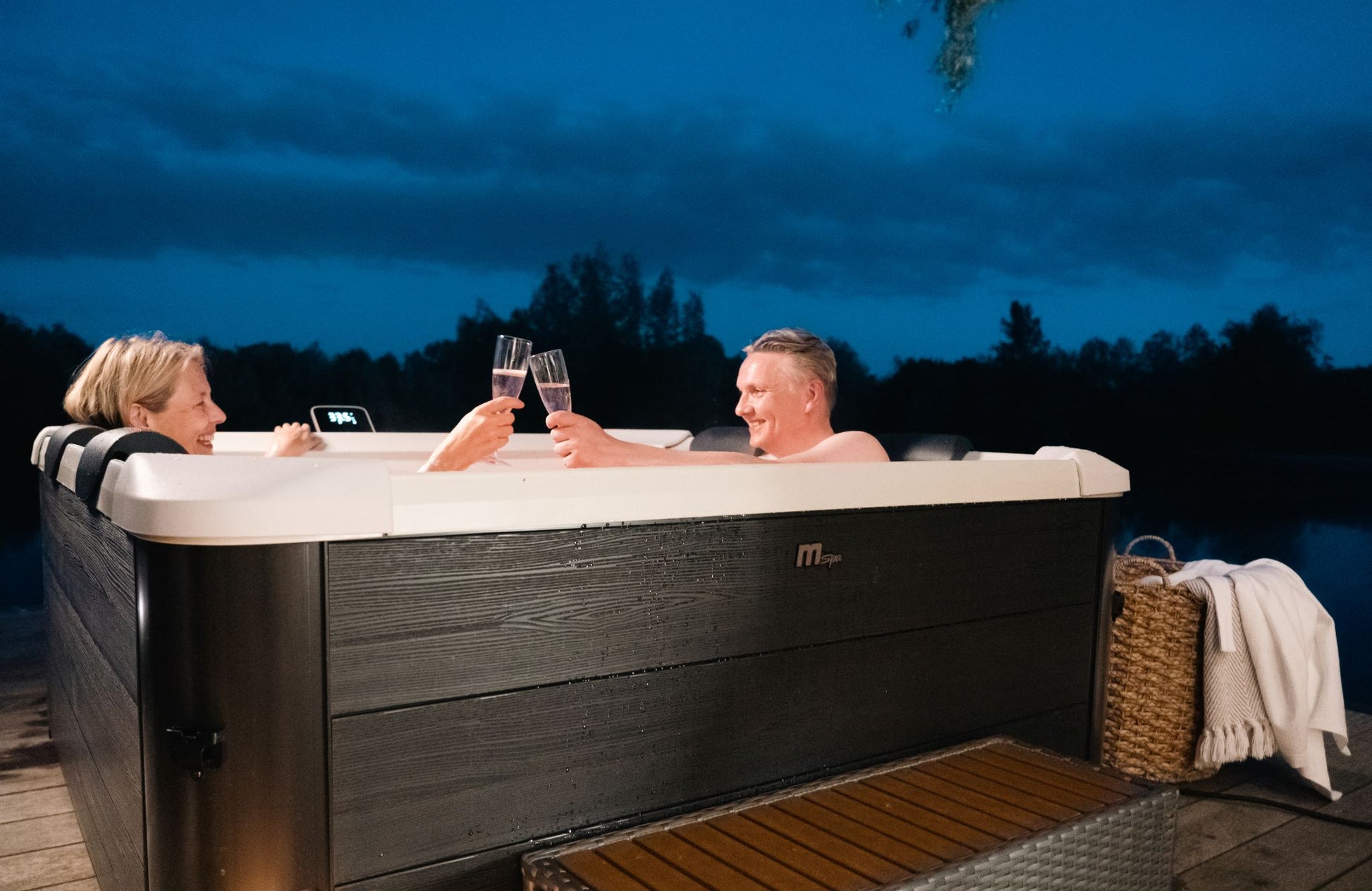 Two people in a hot tub by a lake at night