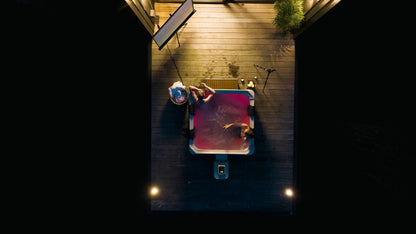 Two people sitting on a hot tub in a backyard at night.