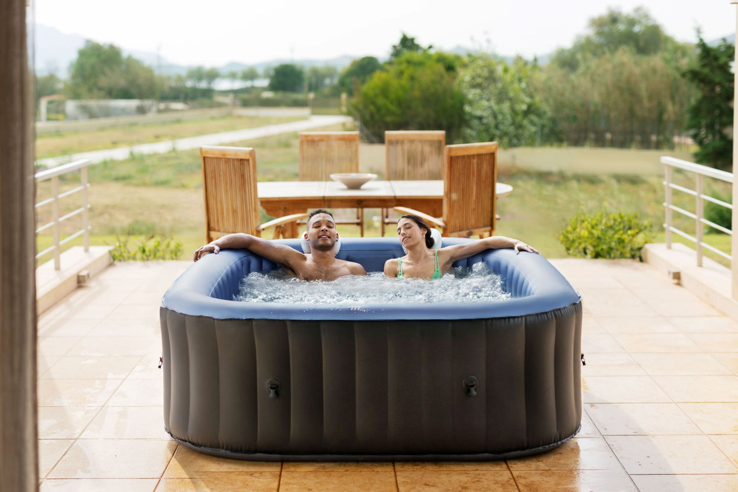 MSpa Two people relaxing in an inflatable hot tub on a patio with a scenic background.  - Luxe Tub Source
