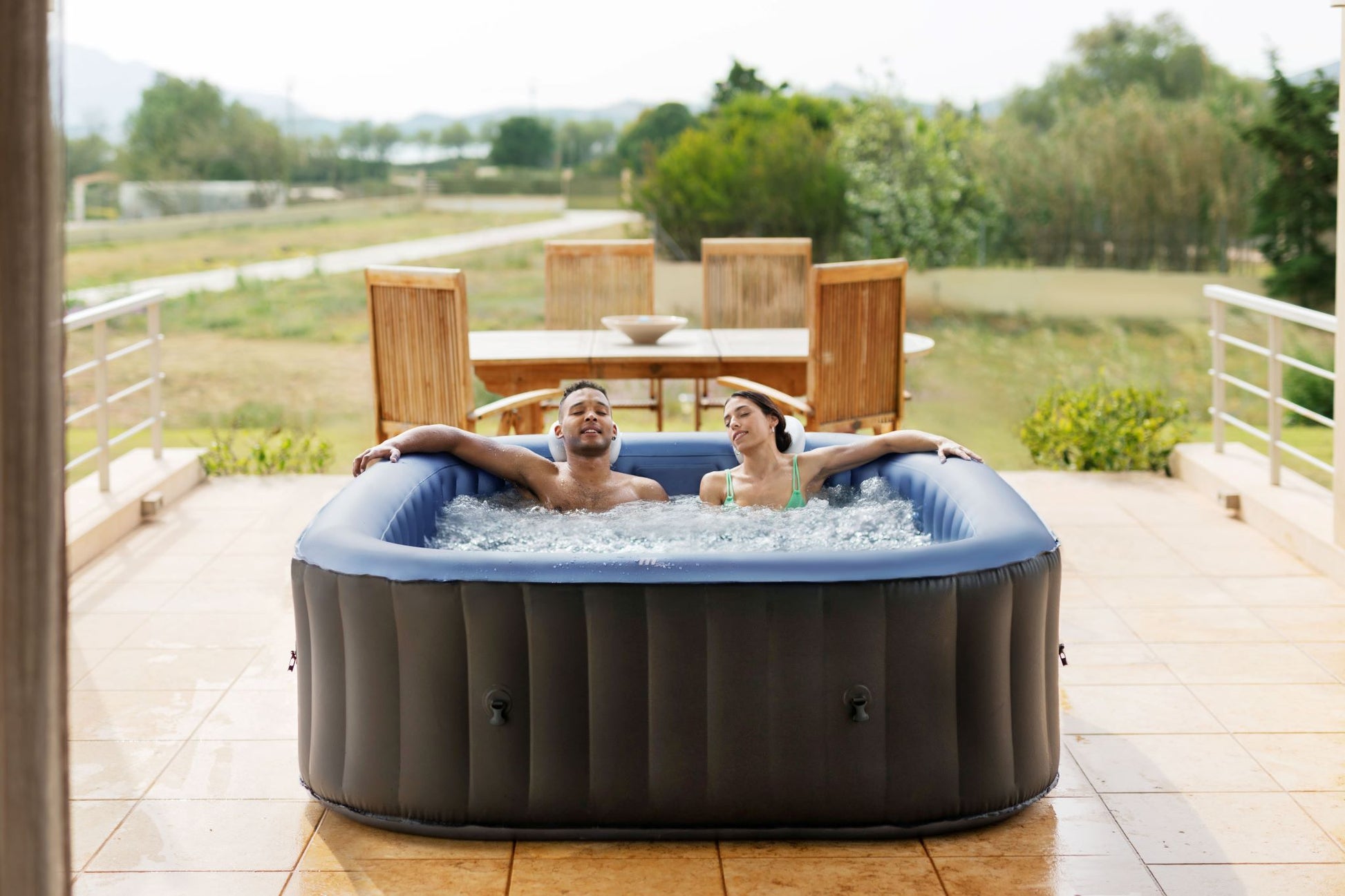 MSpa Two people relaxing in an inflatable hot tub on a patio with a scenic background.  - Luxe Tub Source