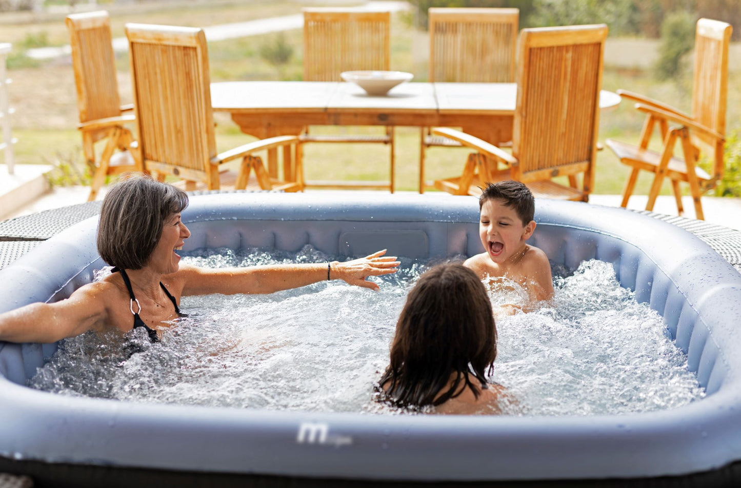 MSpa Family enjoying a hot tub outdoors with wooden furniture and greenery in the background.  - Luxe Tub Source