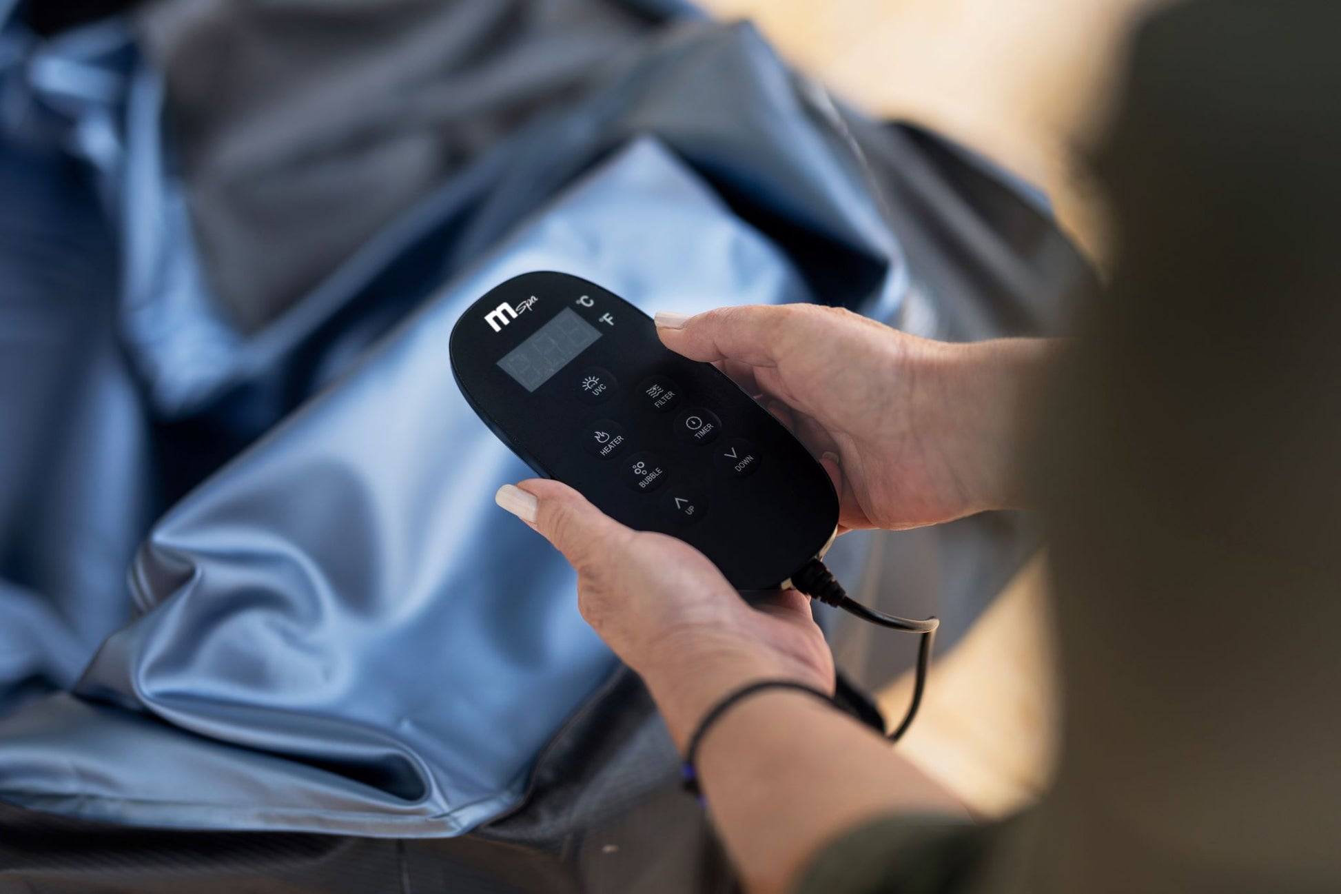MSpa Person holding a black remote control for an inflatable hot tub.  - Luxe Tub Source