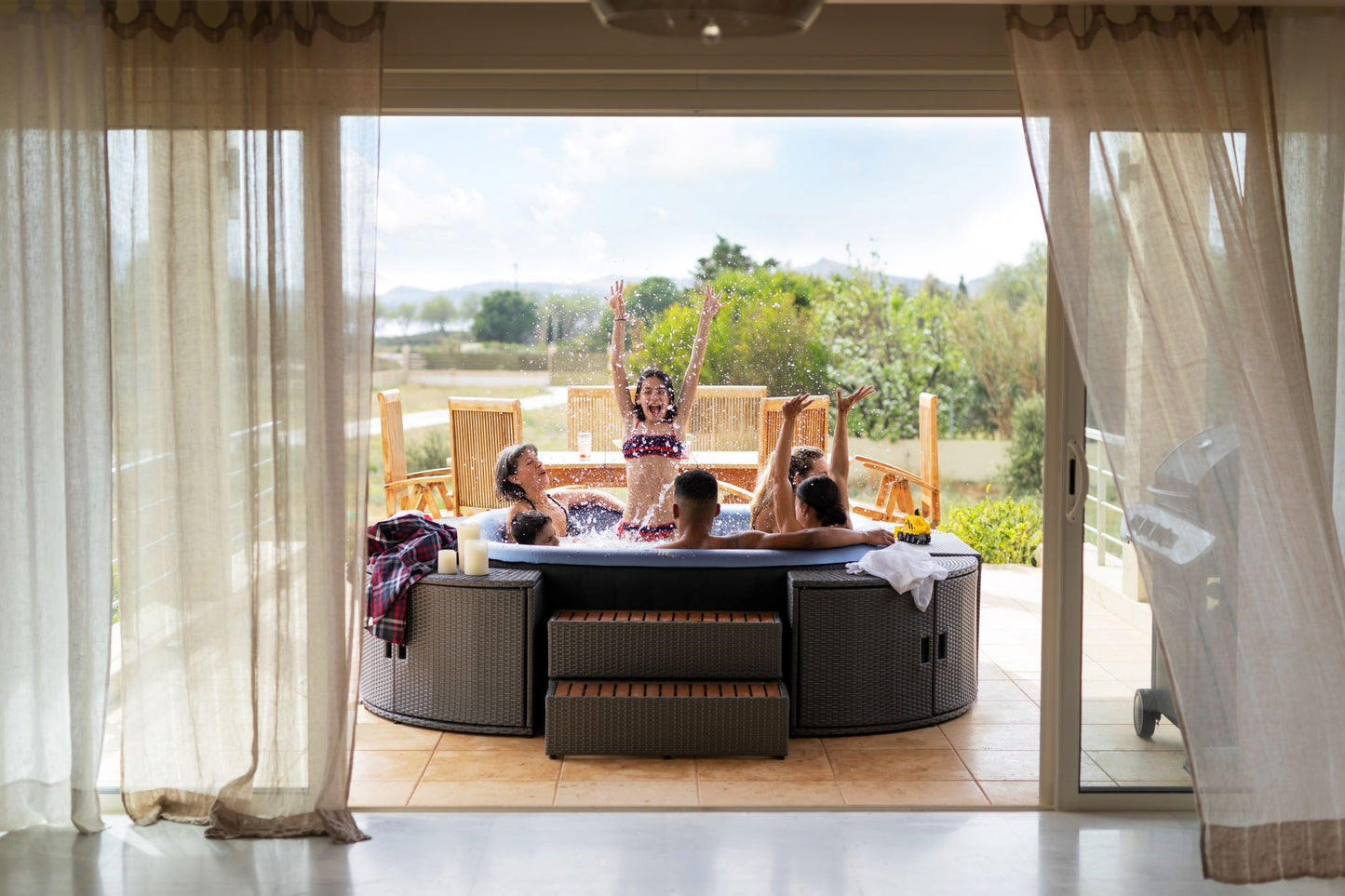 MSpa People splashing water in a hot tub on a patio with a scenic view.  - Luxe Tub Source
