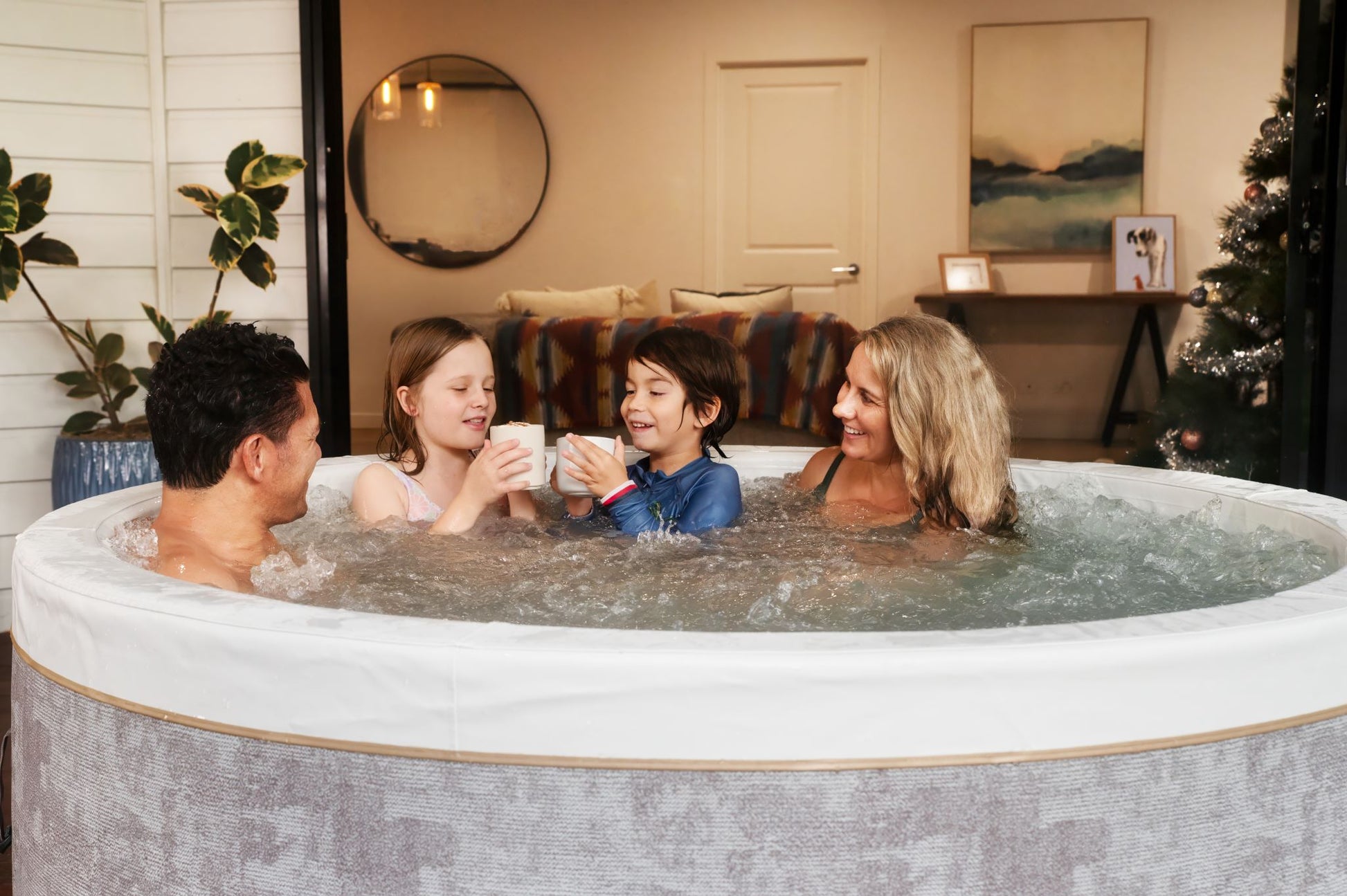 MSpa Family of four in a hot tub in a cozy living room setting. - Luxe Tub Source