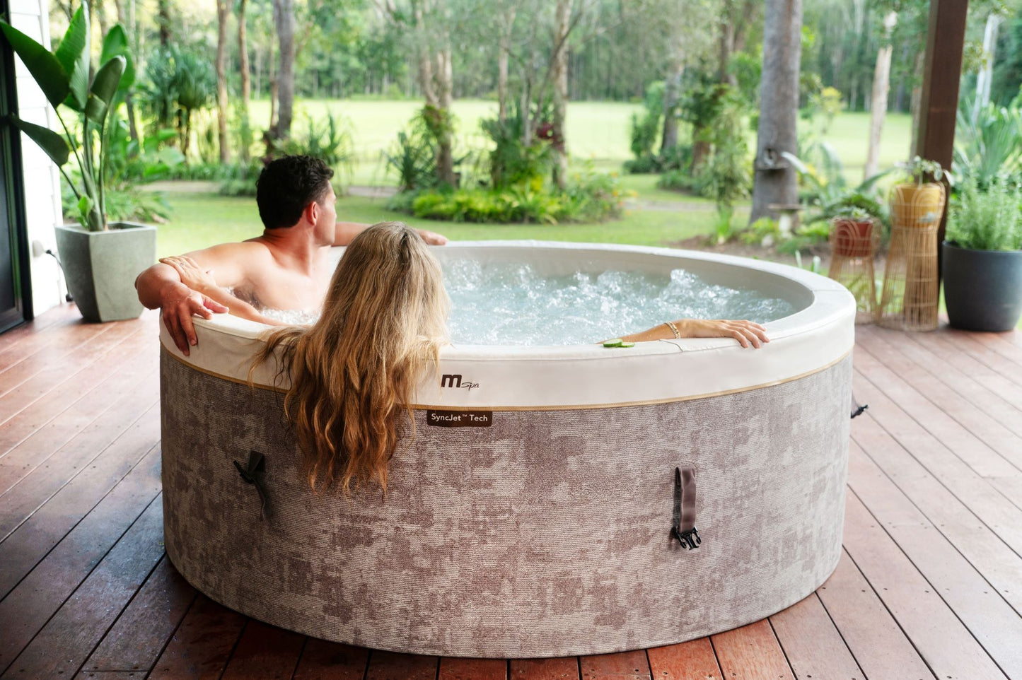 MSpa Two people in a hot tub outdoors with a garden view. - Luxe Tub Source