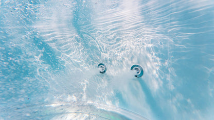 Two hot tub jets submerged in clear blue water with water bubbles.
