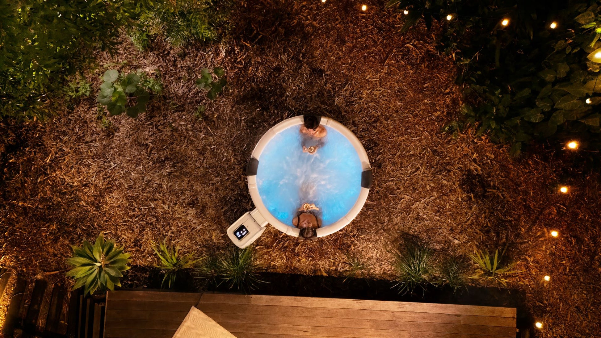 Two people in a hot tub surrounded by nature at night.