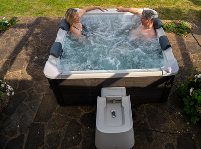 Two people in a hot tub outdoors on a stone patio.
