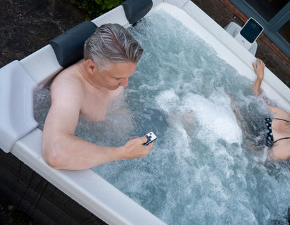 Two people in a hot tub with one using the hot tub remote.