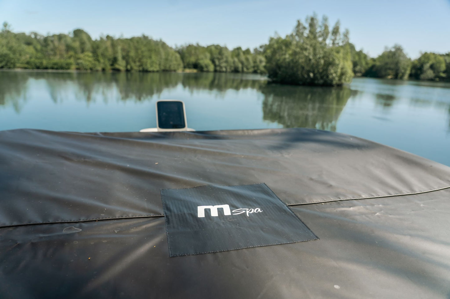 Black cover with 'mSpa' logo on a dock by a lake