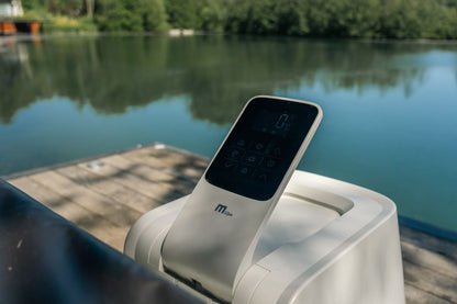 Touchscreen remote control device on a hot tub with a lake in the background.