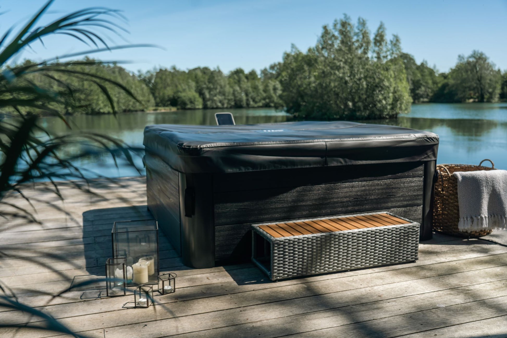 Hot tub on a wooden deck by a lake with trees in the background